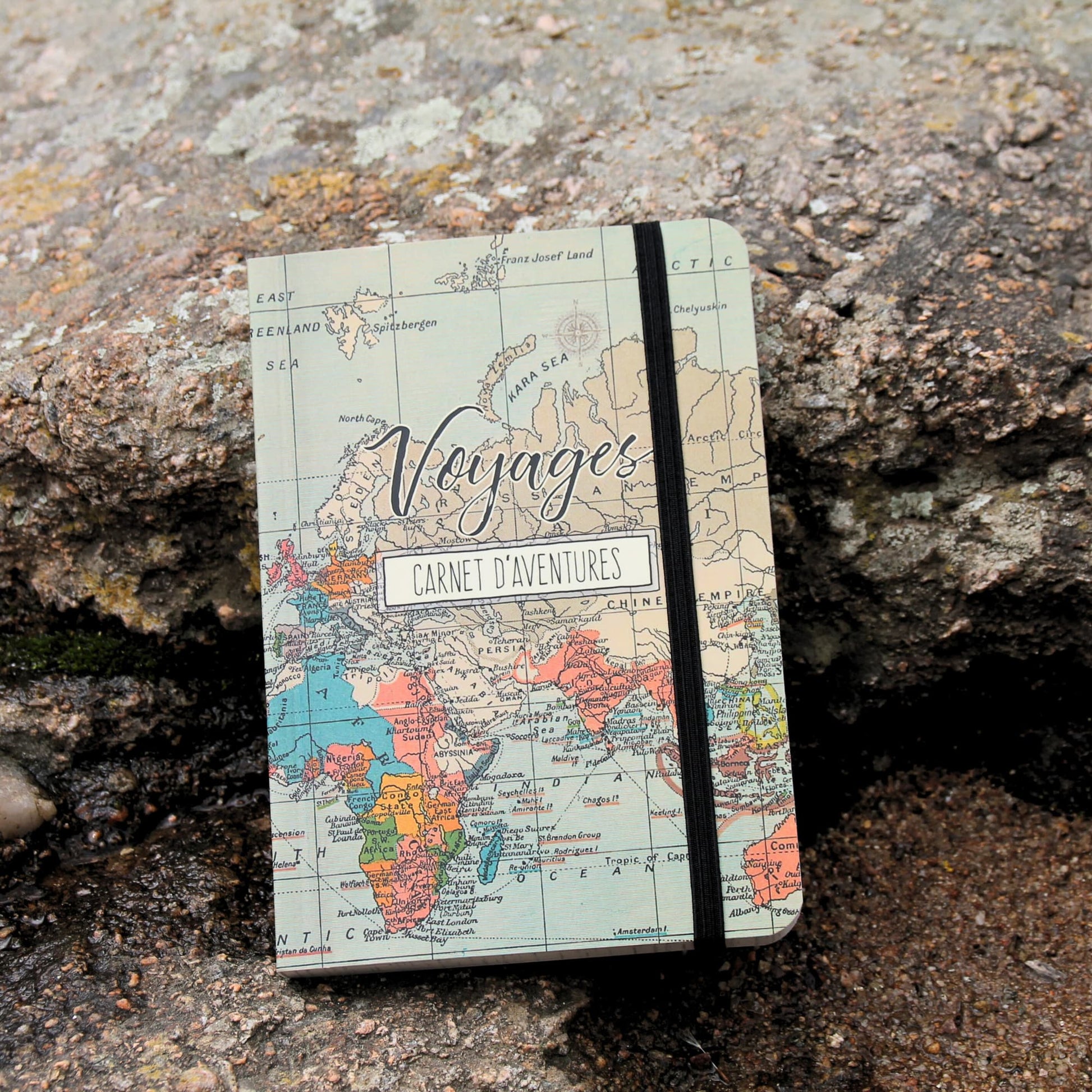 Vue sous un autre angle du carnet de voyage fermé, mettant en avant son design compact et son élastique de fermeture. Son illustration est une véritable invitation au voyage !