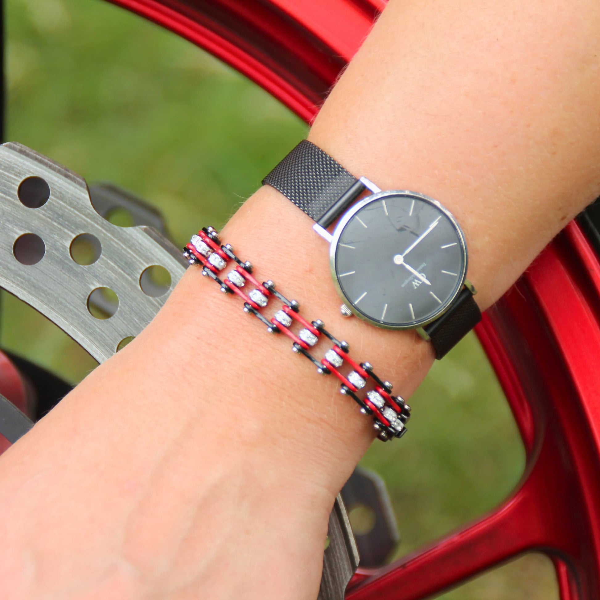 Zoom sur le bracelet chaine moto miniz rouge et zircons pour femme devant une jante de moto.