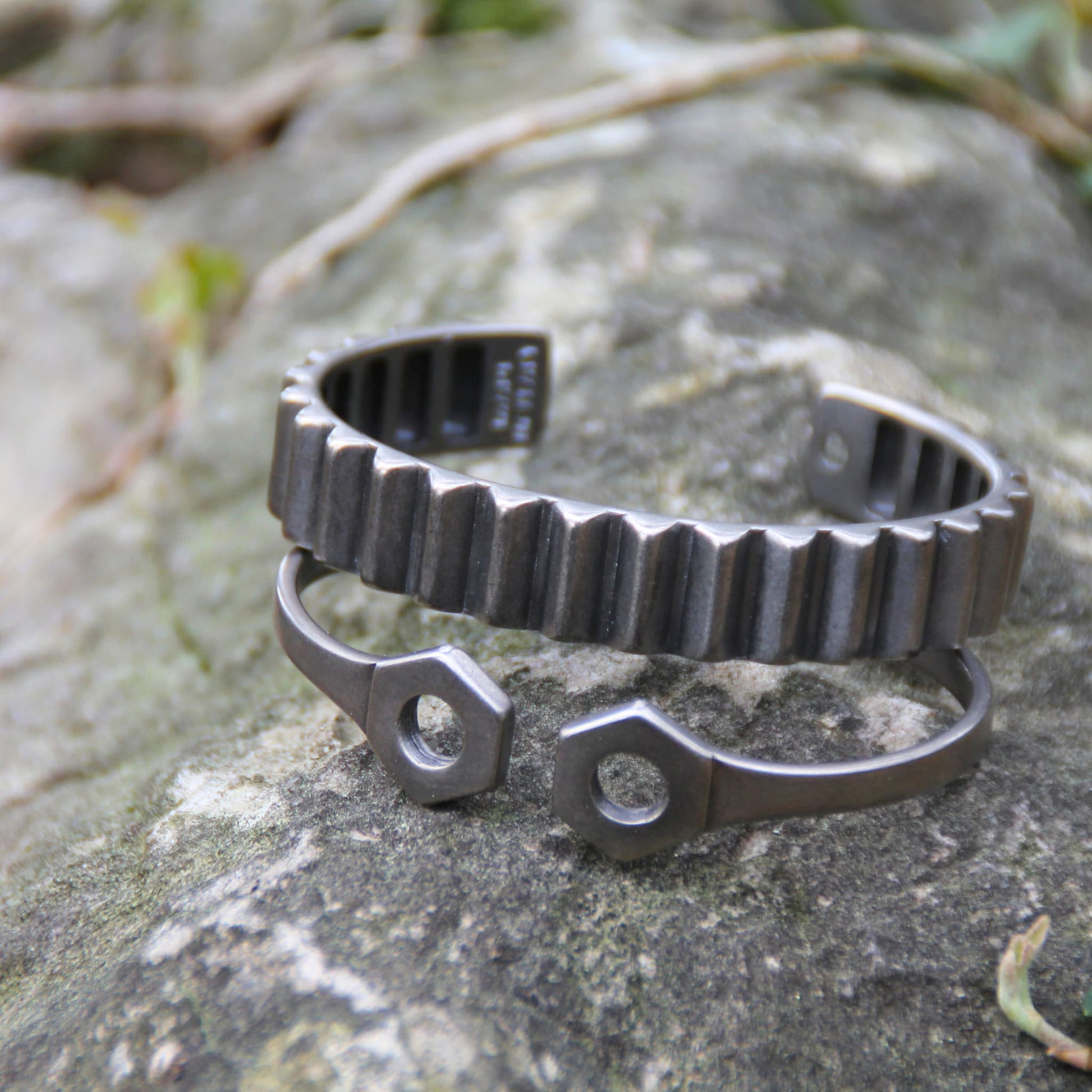Deux bracelets joncs en acier inoxydable argenté de la marque Rouille – Un design inspiré d’un engrenage et d’une double clé plate pour un look audacieux.