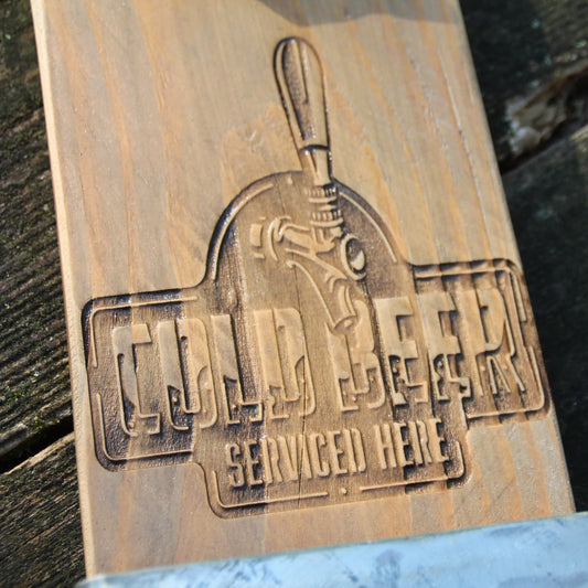 Zoom sur la gravure "Cold Beer Serviced here" du décapsuleur mural en bois.