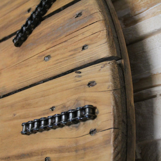 Zoom sur la chaîne de moto entourant l'horloge murale en bois, ajoutant une touche industrielle et brute.