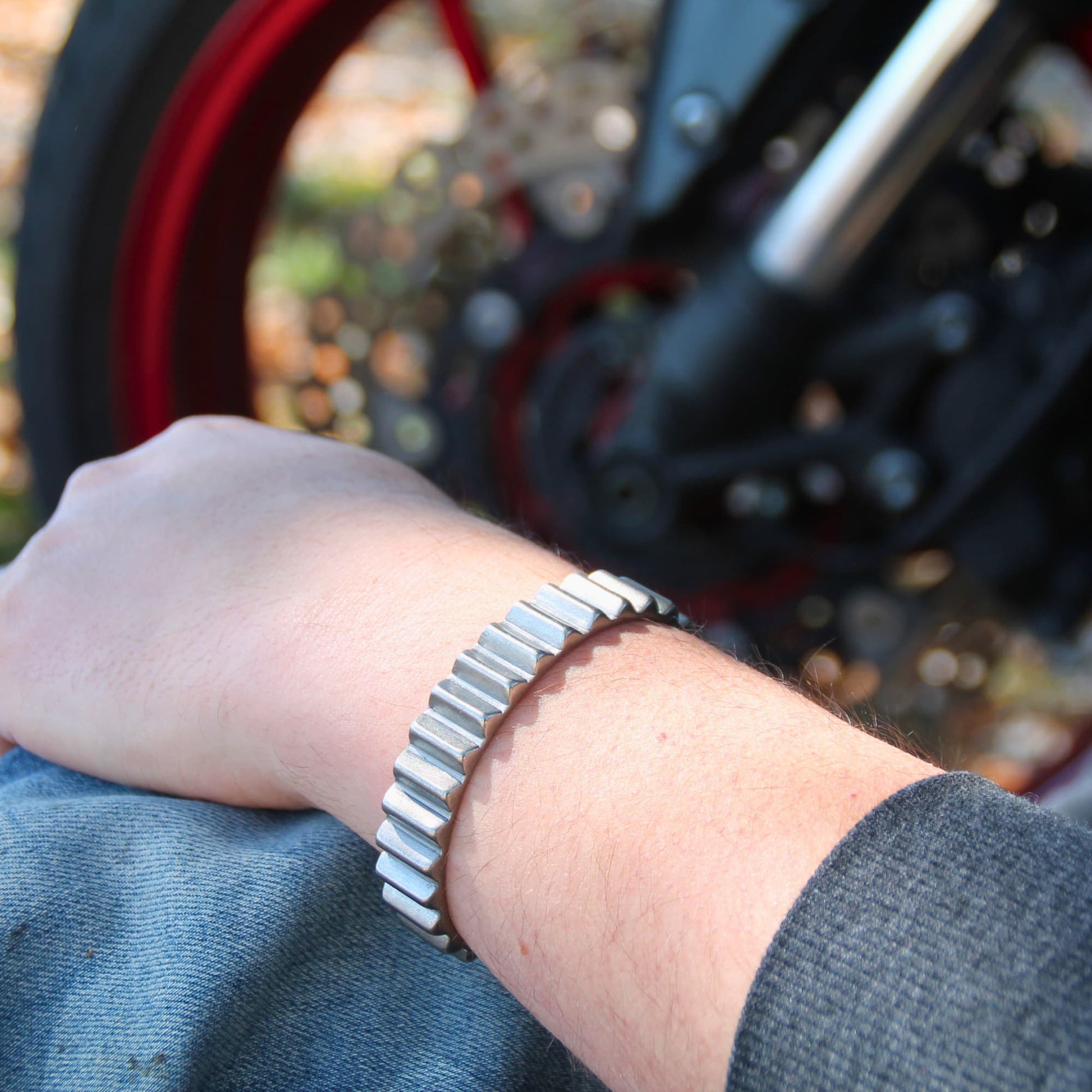 Bracelet jonc 'Gear' en acier inoxydable de la marque italienne Rouille porté par un homme devant une moto. Design inspiré d'un engrenage mécanique.