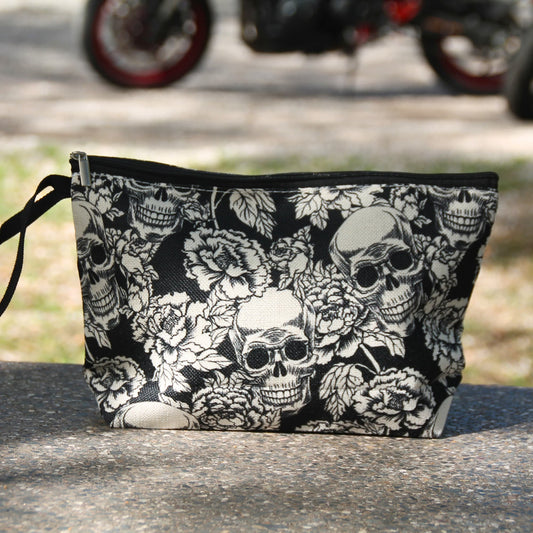 Pochette noire à crânes blancs et roses présentée devant une moto, idée cadeau pour motarde au style rock.