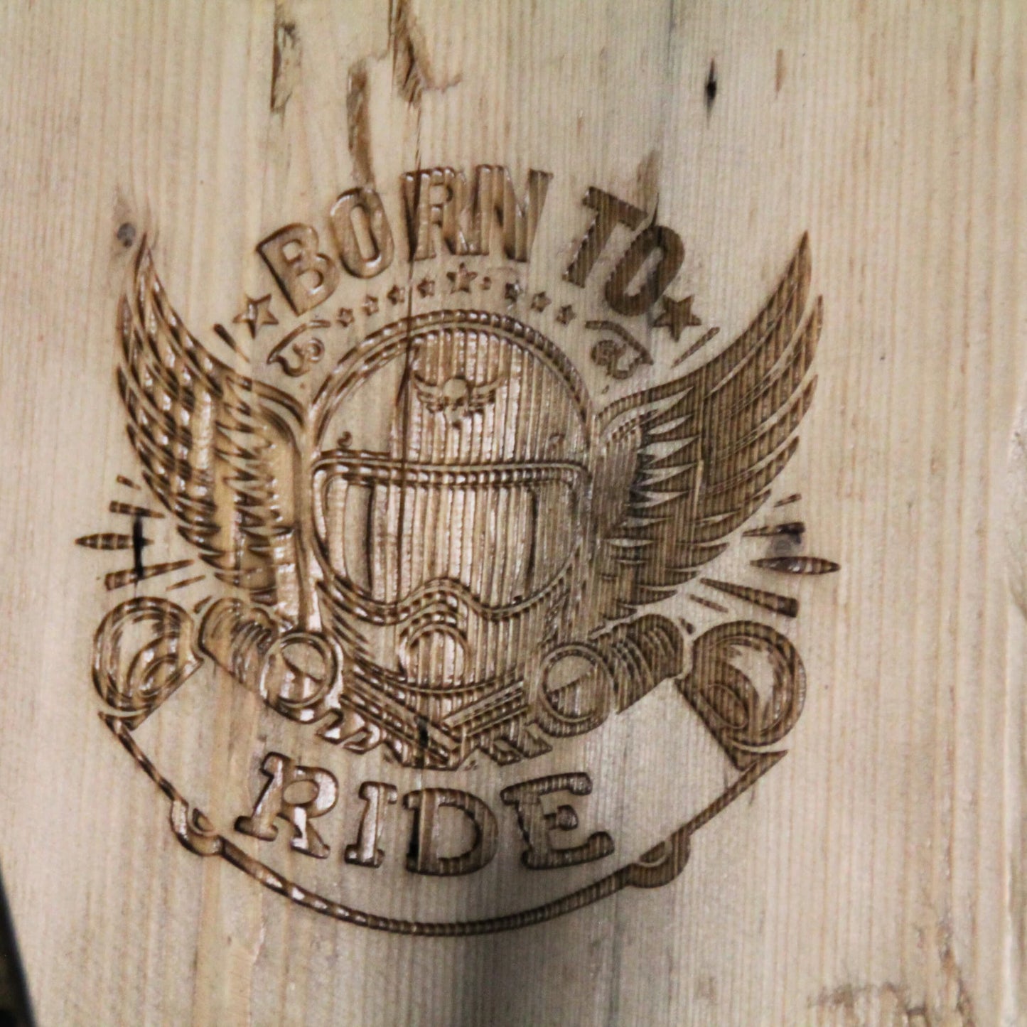 Zoom sur la gravure 'Born to Ride' (né pour rouler) du support de casque moto artisanal en bois, symbolisant la passion de la moto.