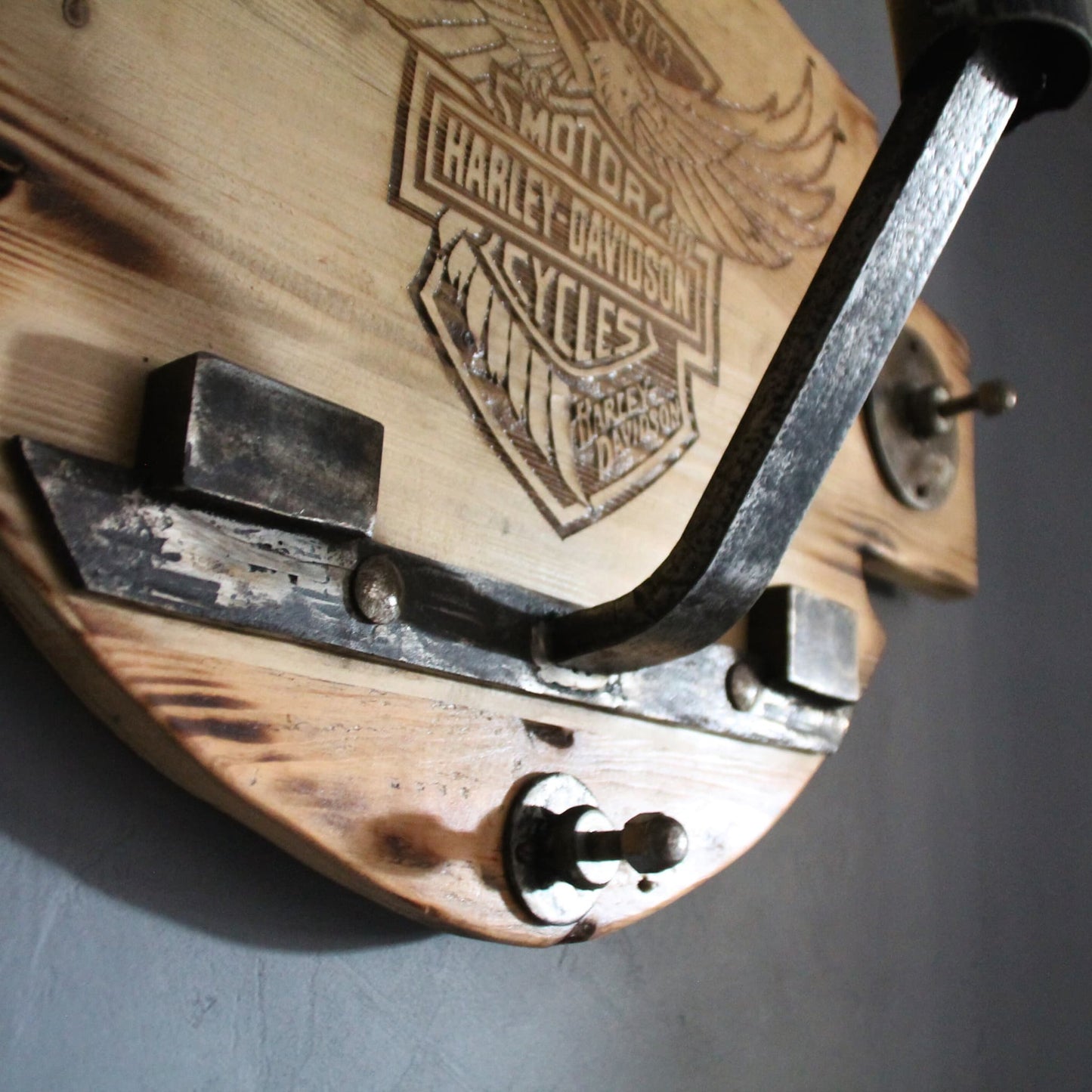 Détail en métal, de pièces mécaniques recyclées, qui composent le support de casque en bois gravé Harley Davidson.