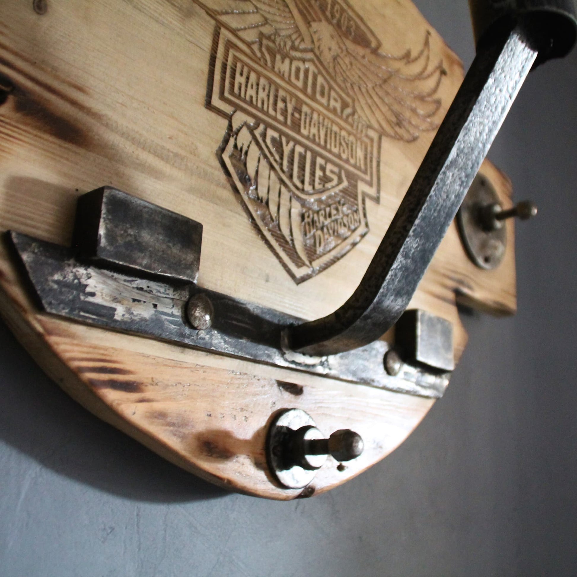 Détail en métal, de pièces mécaniques recyclées, qui composent le support de casque en bois gravé Harley Davidson.