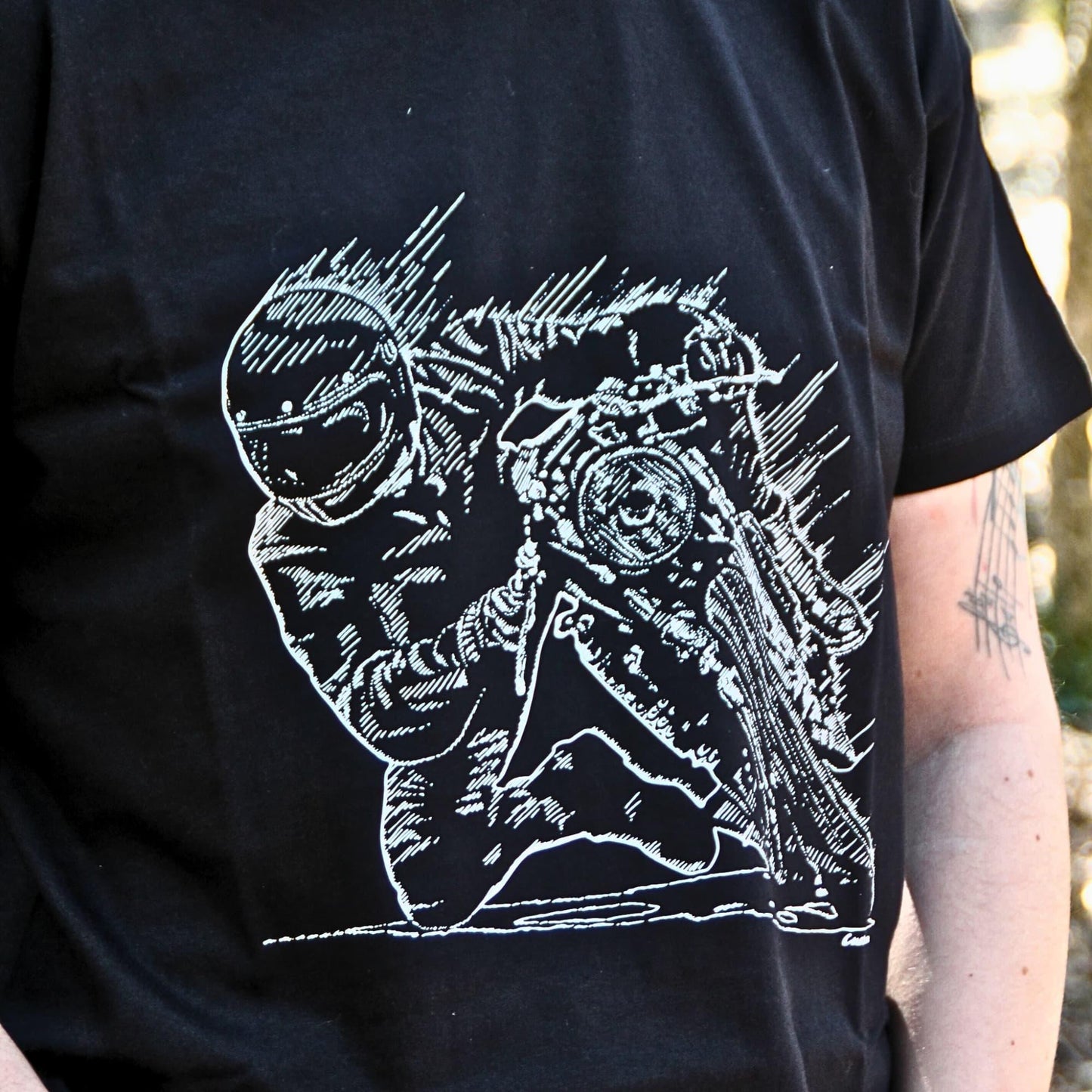 Gros plan sur l'illustration d'un pilote en pleine prise d’angle, genou au sol, imprimée sur un t-shirt en coton noir. Un design détaillé pour les passionnés de vitesse et de pilotage.