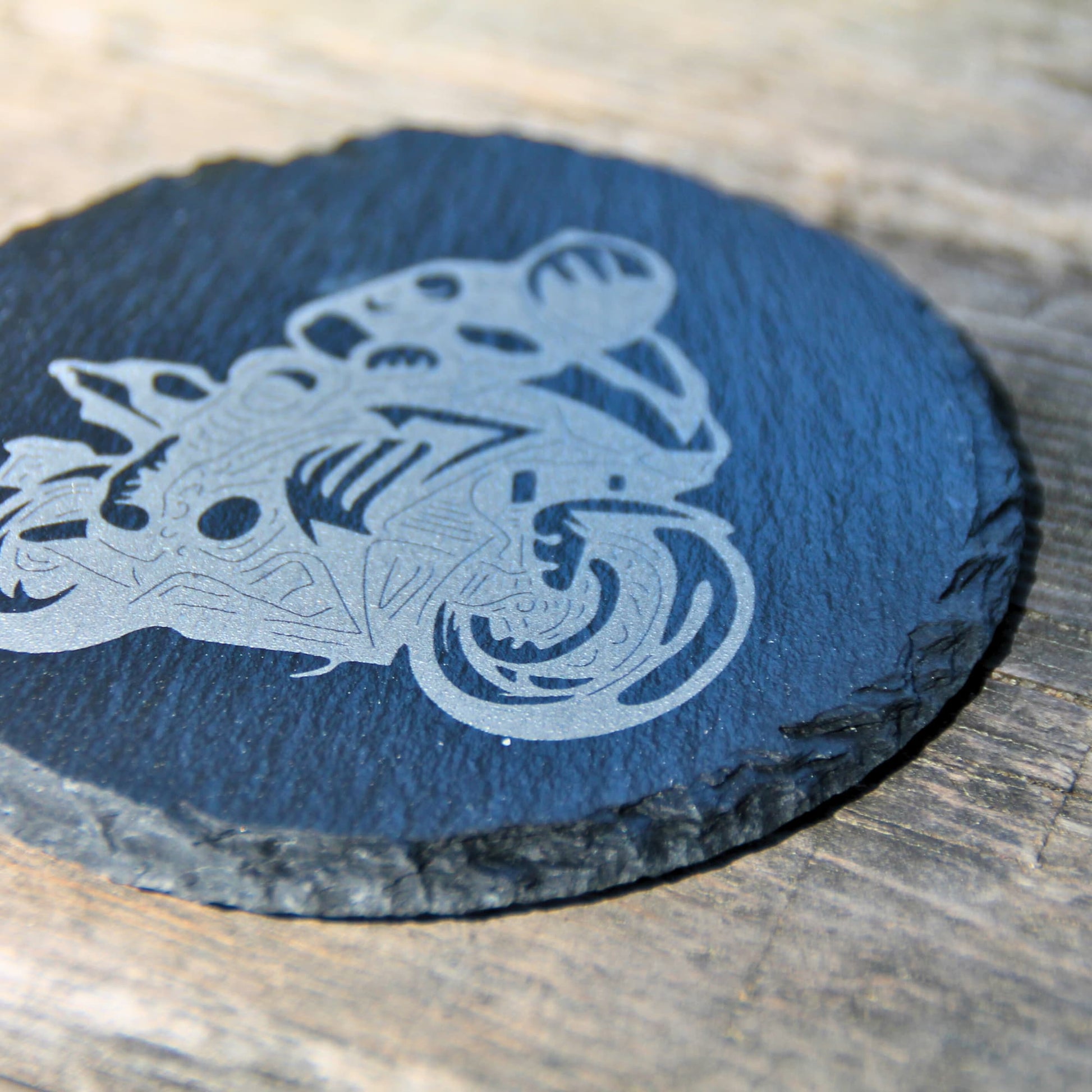 Zoom sur le dessous de verre en ardoise naturelle gravé d'un motard sur sa moto.