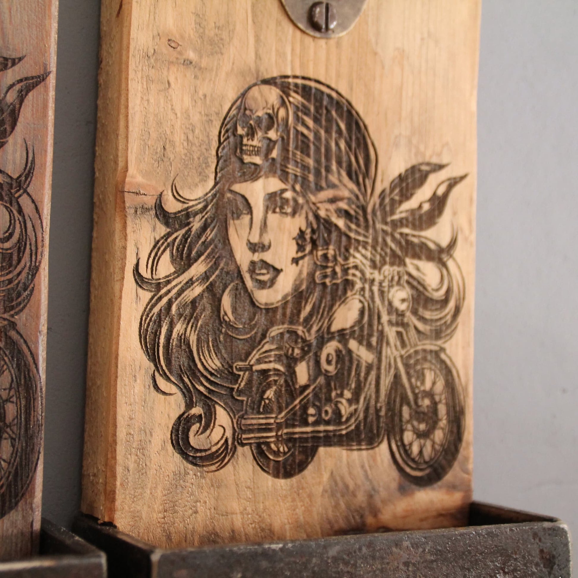 Zoom sur la gravure du décapsuleur mural bois clair. Gravure pirate motarde sexy.