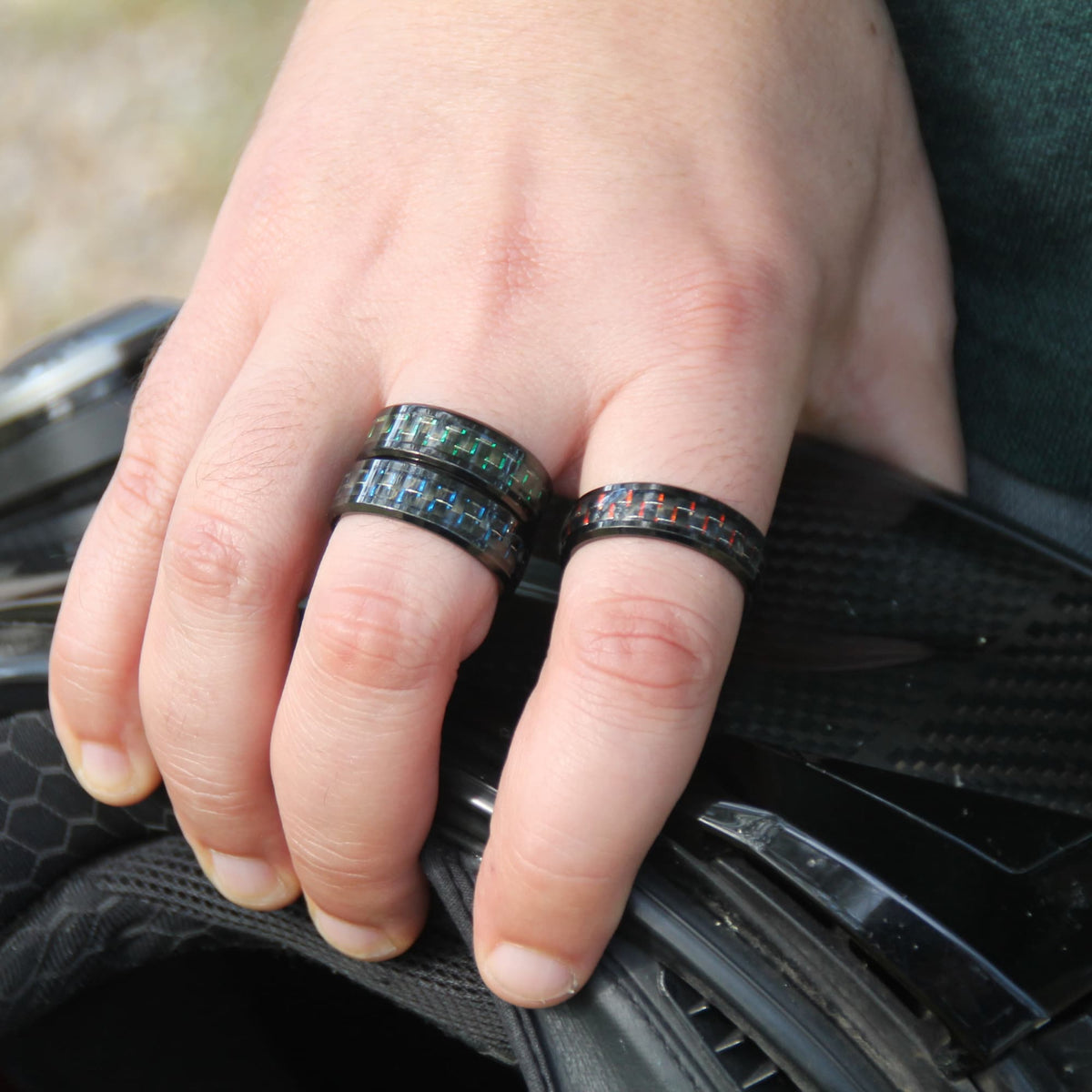 Trio de bagues motard en acier inox noir et fibre de carbone colorée portées par un motard tenant son casque carbone