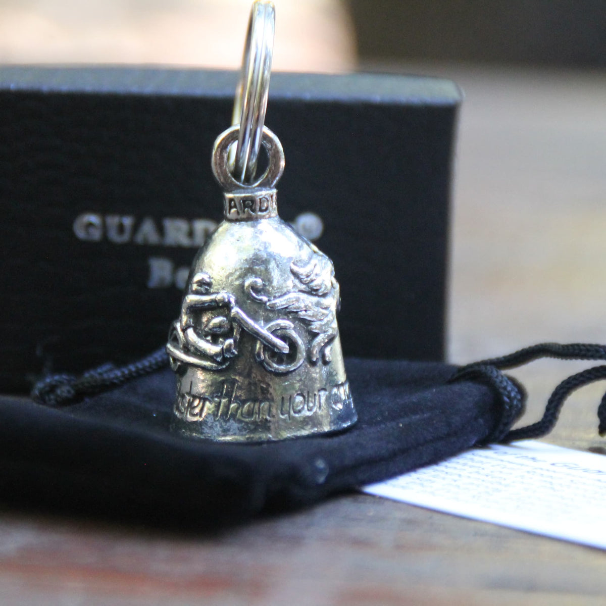 Clochette Guardian Bell ange et motard posée sur sa pochette en velours noir officielle