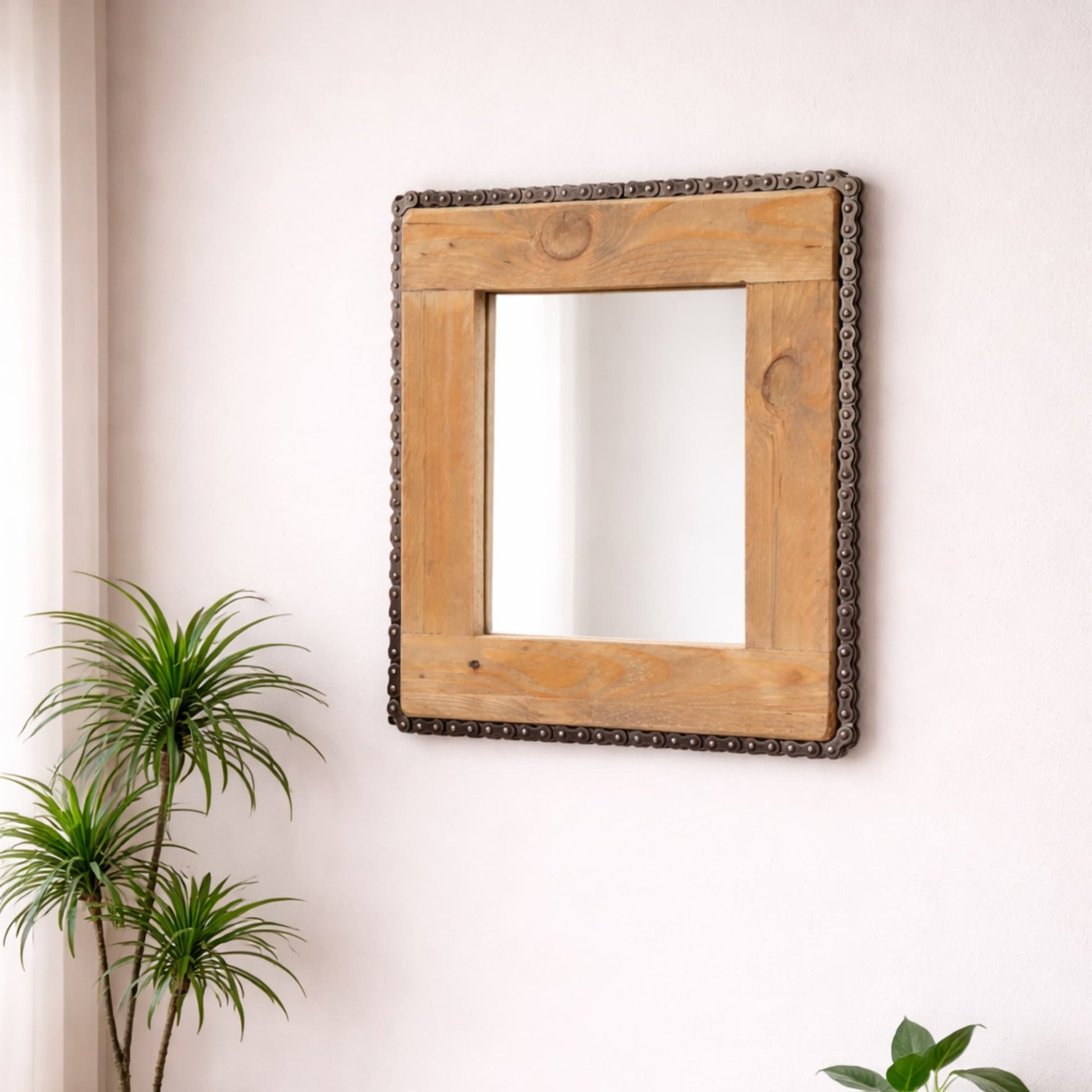 Miroir artisanal en bois brut et chaine de moto recyclée mis en situation sur un mur. 