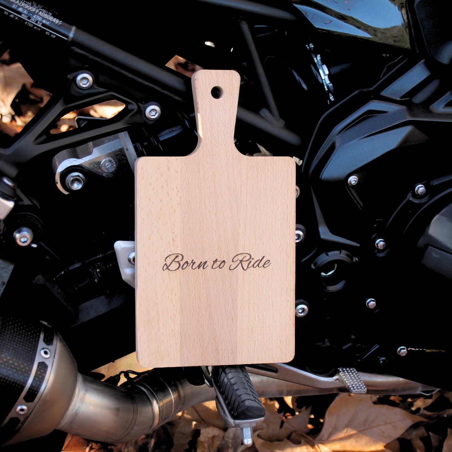 Petite planche à découper en bois gravé Born to Ride, posée sur une moto.