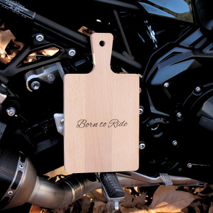 Petite planche à découper en bois gravé Born to Ride, posée sur une moto.