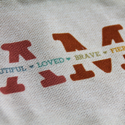 Zoom sur le tissu imitation lin et les lettres colorées de la pochette Je suis forte, belle…