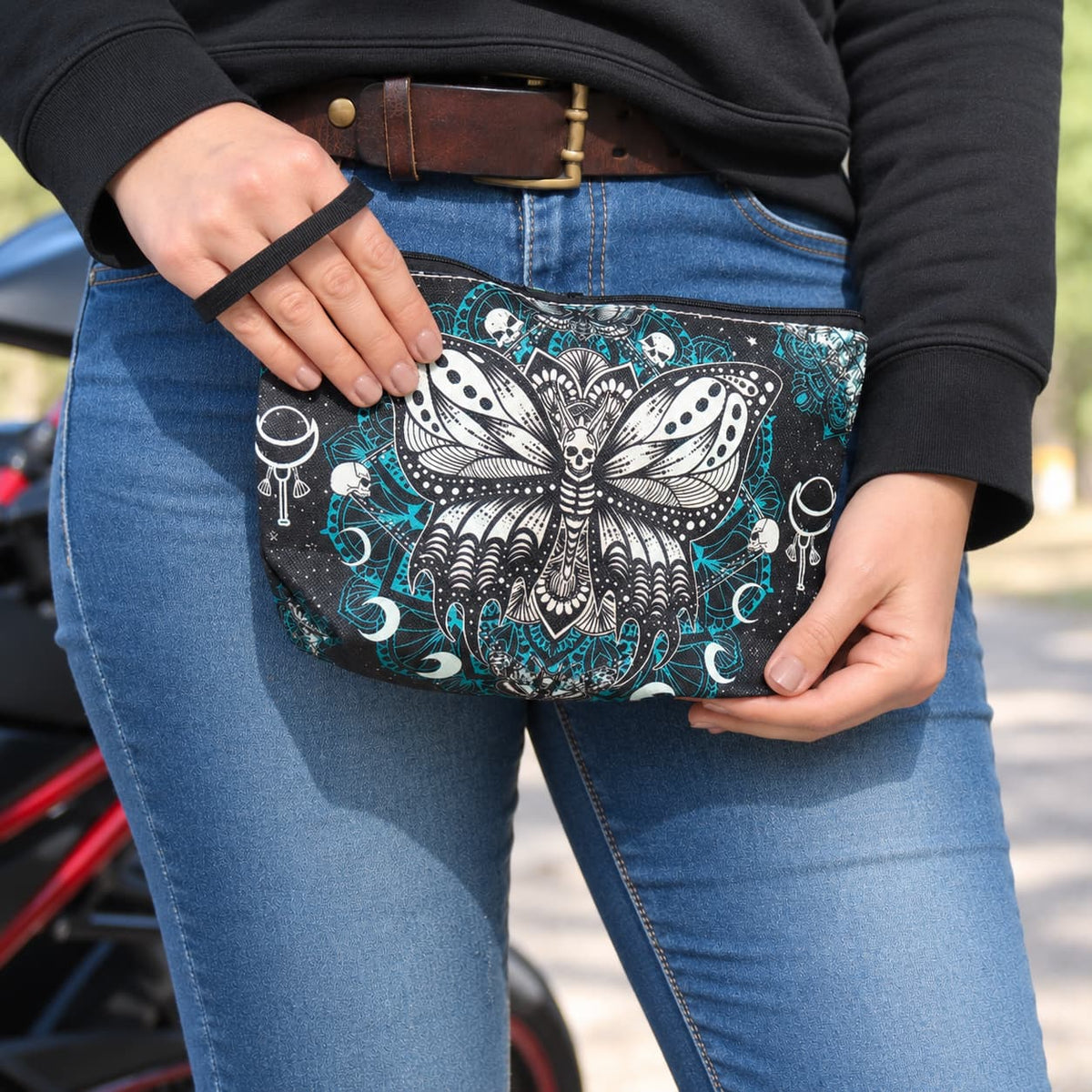 Pochette biker Papillon Mandala tenue entre les mains, motif noir, blanc et turquoise. idéale pour maquillage et petits objets