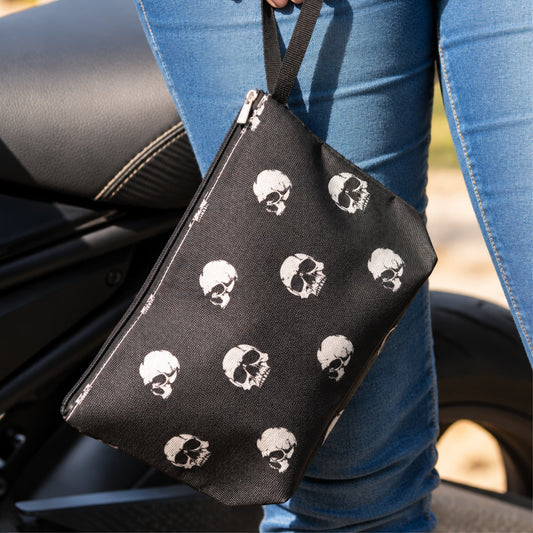 Pochette biker noire à crânes blancs tenue par sa dragonne.