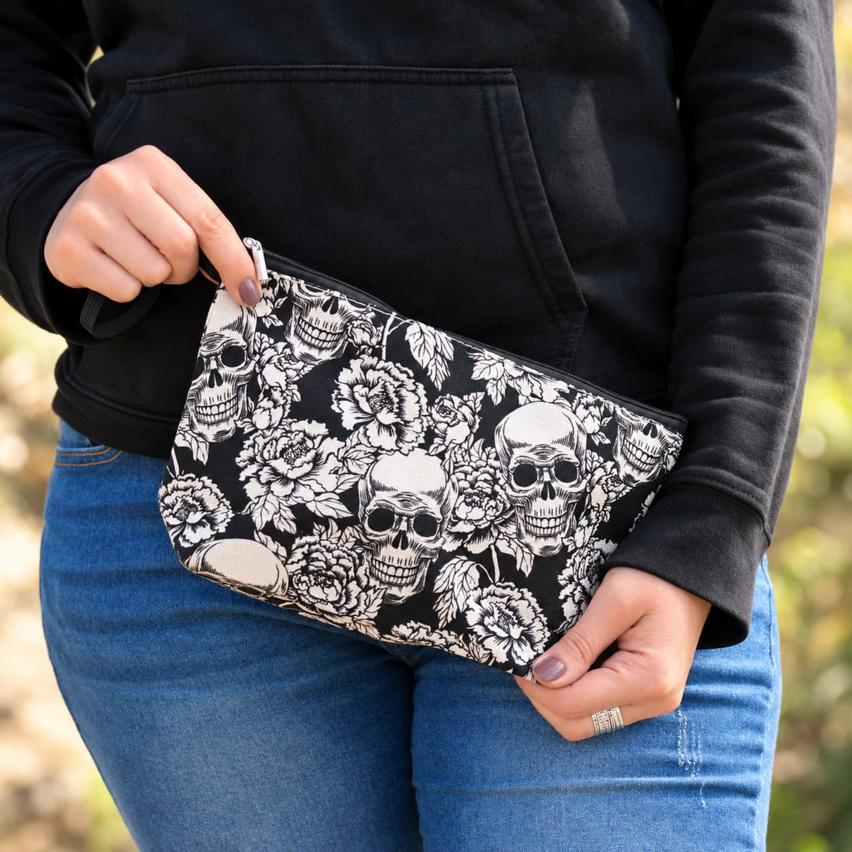 Pochette noire à imprimé floral et crânes blancs tenue en mains, accessoire rock pour motarde.