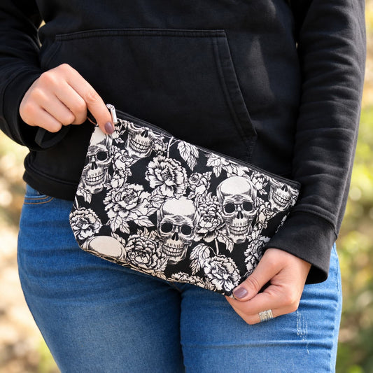 Pochette noire à imprimé floral et crânes blancs tenue en mains, accessoire rock pour motarde.