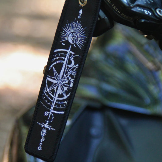 Porte clé moto en tissu noir brodé de symboles evoquant le voyage et l'évasion (rose des vents, soleil, oiseaux...) 