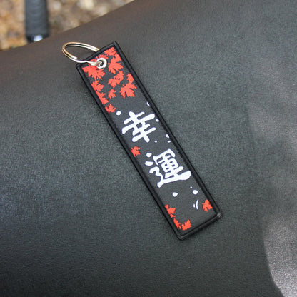 Porte clé en tissu brodé de caractères japonais signifiant Chance / Fortune, avec des feuilles d'erables rouges