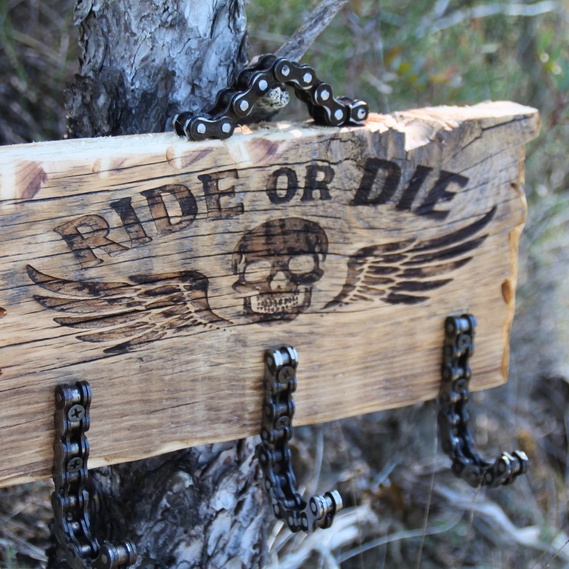 Détail de la gravure Ride or Die avec tête de mort ailée sur porte-clé mural en bois style biker