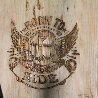 Zoom sur la gravure 'Born to Ride' (né pour rouler) du support de casque moto artisanal en bois, symbolisant la passion de la moto.