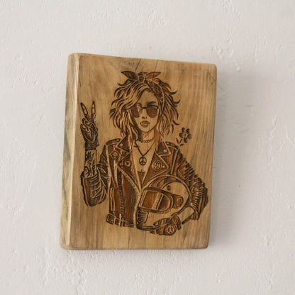 Tableau artisanal en bois brut et gravure motarde signe V sur mur blanc