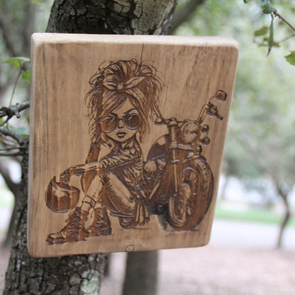 Tableau artisanal en bois gravé d'une motarde caricaturale. Fait main dans les alpes maritimes