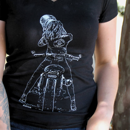 T-shirt motarde femme en coton noir, imprimé avec un visuel dynamique d’une motarde en train de retirer son casque après une aventure à moto.