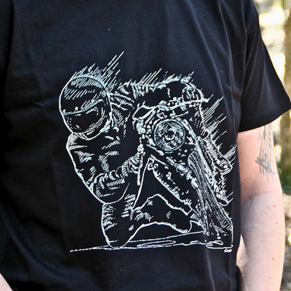 Gros plan sur l'illustration d'un pilote en pleine prise d’angle, genou au sol, imprimée sur un t-shirt en coton noir. Un design détaillé pour les passionnés de vitesse et de pilotage.