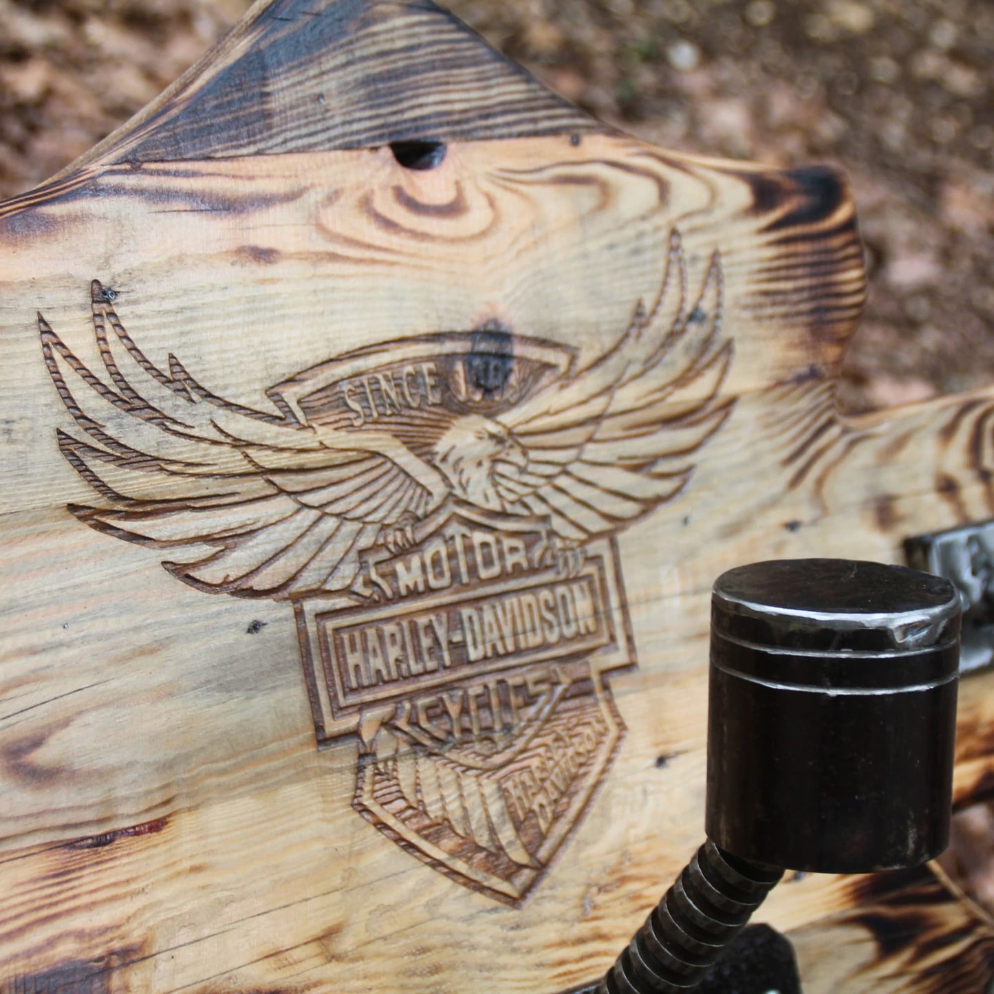 Gros plan gravure profonde logo Harley Davidson sur porte casque moto mural bois brûlé – détail relief saisissant et effet old-school biker artisanal