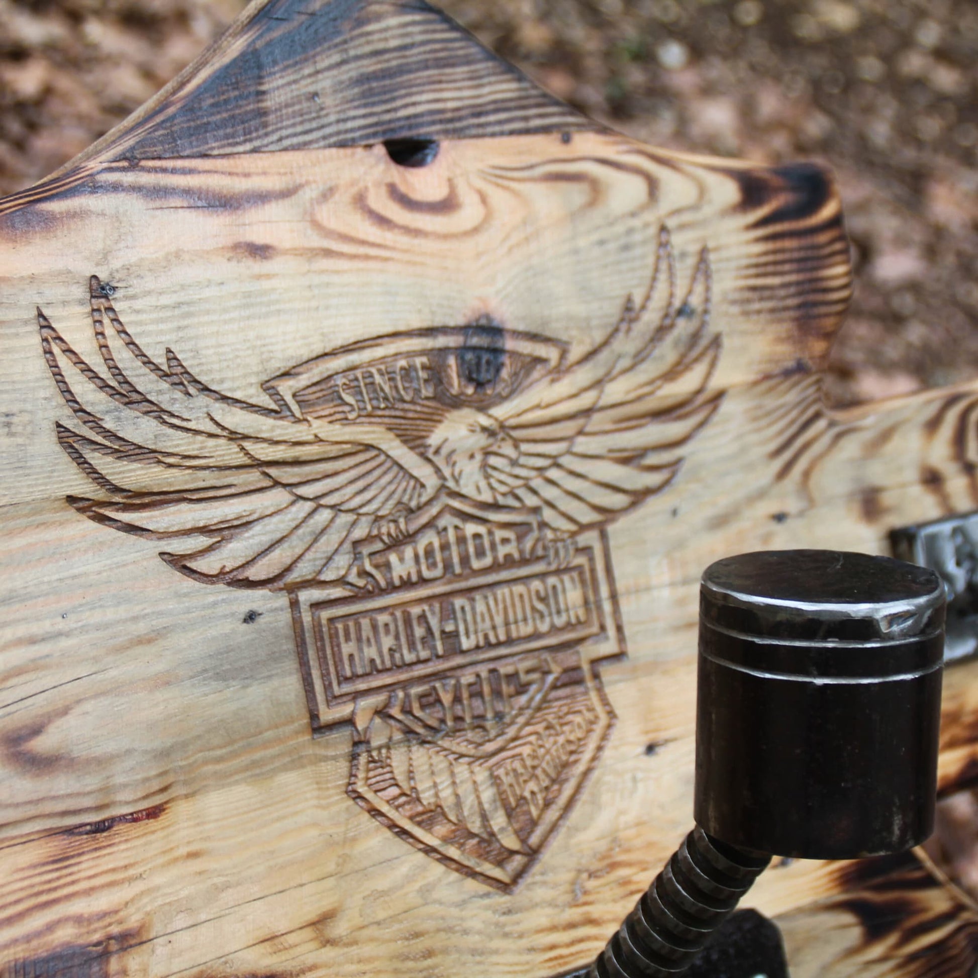 Gros plan gravure profonde logo Harley Davidson sur porte casque moto mural bois brûlé – détail relief saisissant et effet old-school biker artisanal