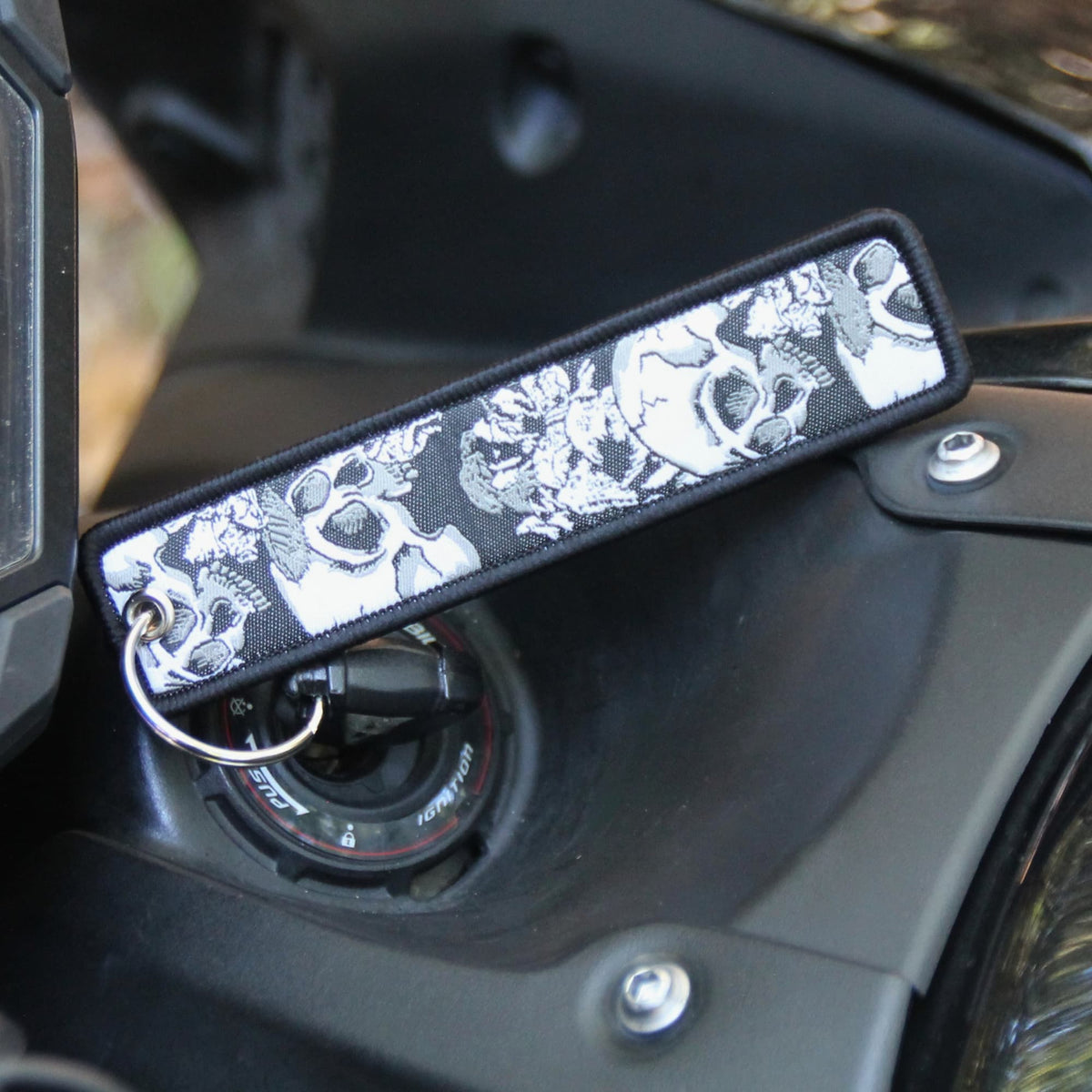 Zoom sur le Porte clé moto en tissu noir brodé de cranes et de fleurs. 