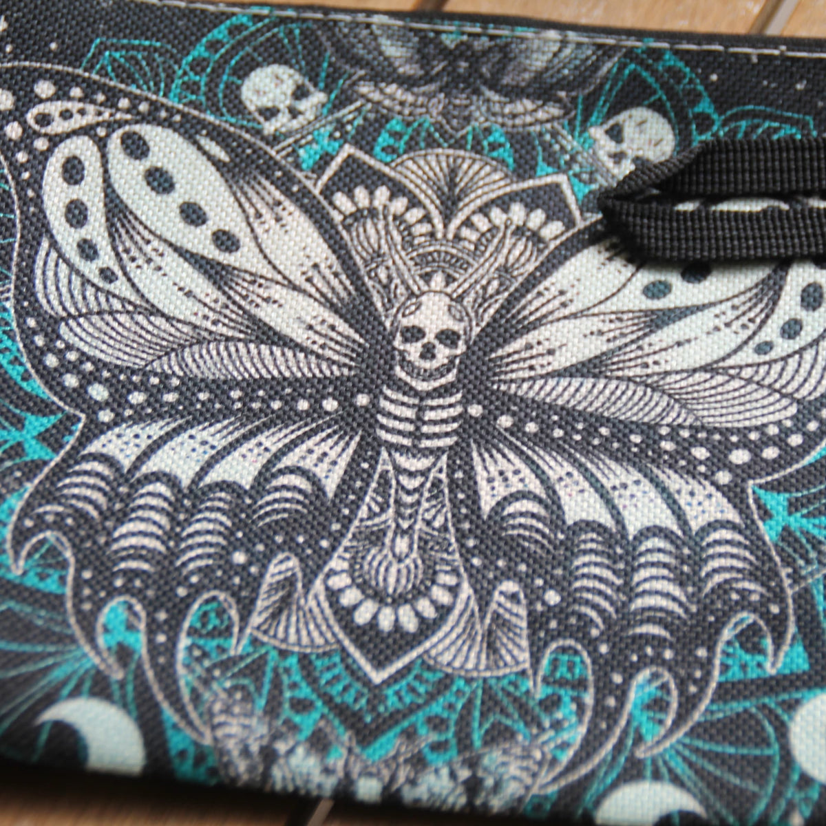 Gros plan sur le motif papillon mandala et les détails turquoise de la pochette motarde rock
